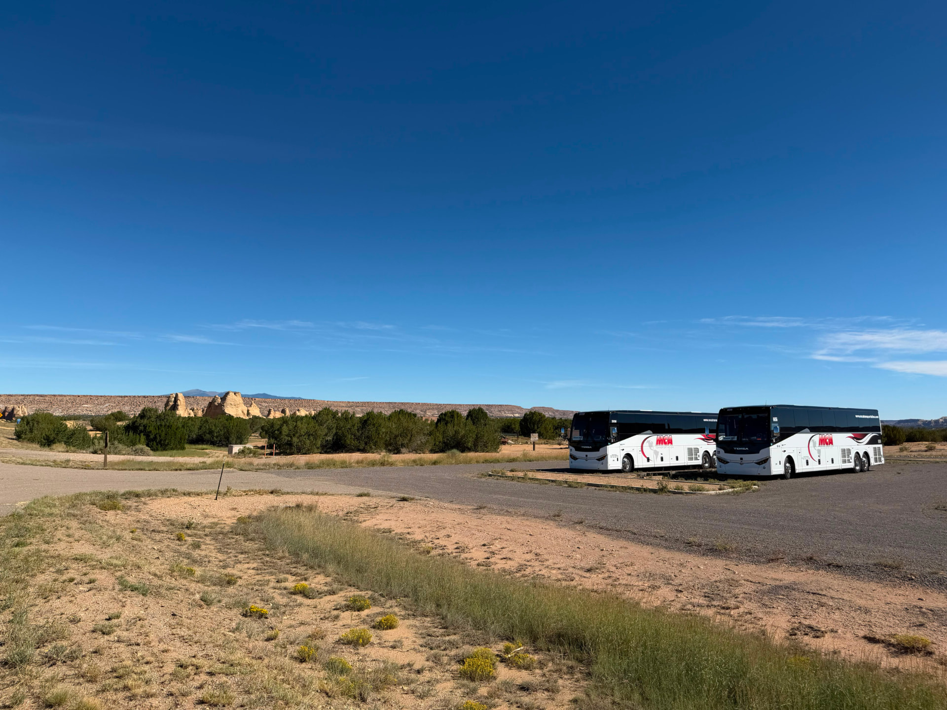 Two MCA Transportation motorcoaches parked at a red rock mesa overlook in New Mexico